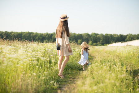 时髦的年轻母亲带着蹒跚学步的女孩在大自然中行走