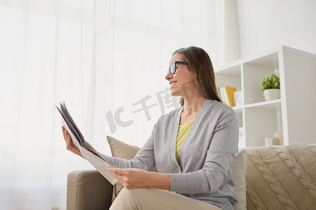 大众媒体和人们的概念—快乐的中年妇女在家读报。快乐的女人在家里读报纸