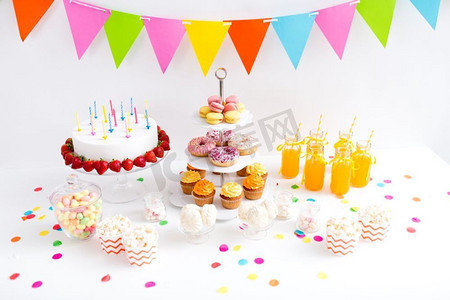 橙色生日摄影照片_派对和节日概念—生日蛋糕，蜡烛和草莓，饮料和食物上桌。生日派对上的食物和饮料