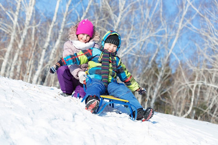 冬天的乐趣。男孩和女孩在美丽的雪地公园玩雪橇