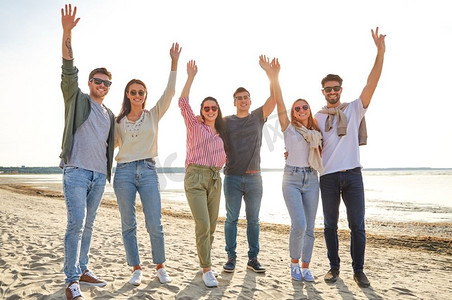 友谊，休闲和人的概念—一群快乐的朋友在海滩上挥手在夏天。快乐的朋友在海滩上挥舞着手在夏天