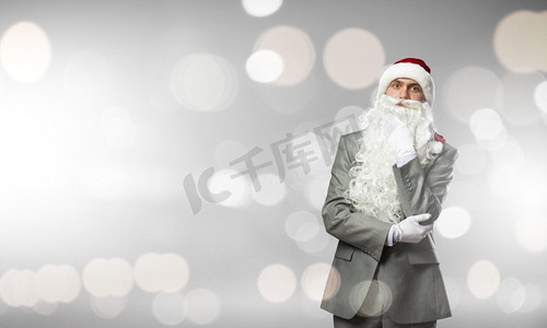圣诞老人帽子摄影照片_商业圣诞老人。戴着圣诞老人帽子，手托着下巴的体贴的商人