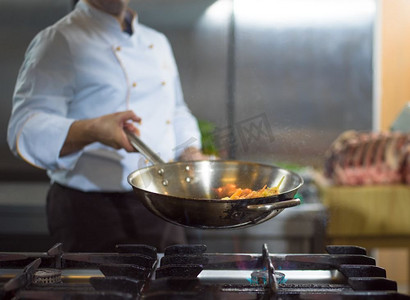 正在做什么摄影照片_厨师在餐厅的厨房里烹饪和制作食物的火焰。厨师在食物上做火焰弹
