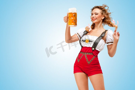 一名年轻性感的瑞士女子穿着红色套头短裤，背带是传统的连衣裙，拿着一个蓝色背景的啤酒杯。