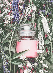 天然化妆品罐，草药叶和野花上有淡粉色奶油，空白标签用于品牌模型，俯视，平铺
