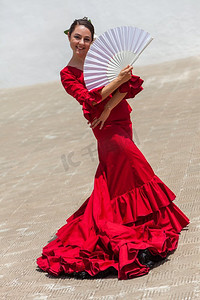 西班牙女摄影照片_西班牙女弗拉门戈舞者穿着红色连衣裙在户外表演，与白色扇子合影