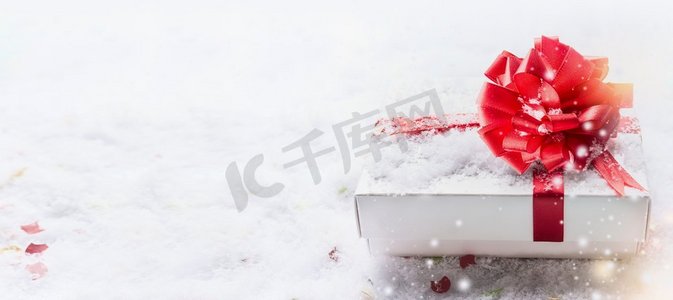 白色礼品盒与红色蝴蝶结在雪与bokeh，旗帜。复制模板，邀请，优惠券，销售和祝贺。