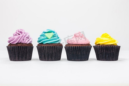 四个巧克力杯蛋糕与糖霜或糖霜，粉红色，紫色，黄色和蓝色与绿叶，拍摄在白色背景