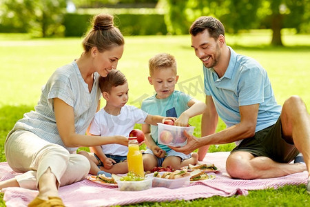 家庭、休闲和人的概念-快乐的母亲、父亲和两个小儿子在夏季公园野餐。快乐的一家人在夏季公园野餐