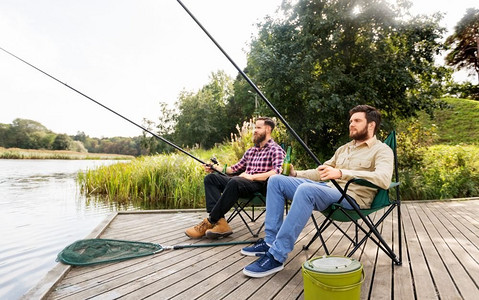 户外喝啤酒摄影照片_休闲与人的概念—男性朋友在湖上钓鱼和喝啤酒。男性朋友钓鱼和喝啤酒在湖