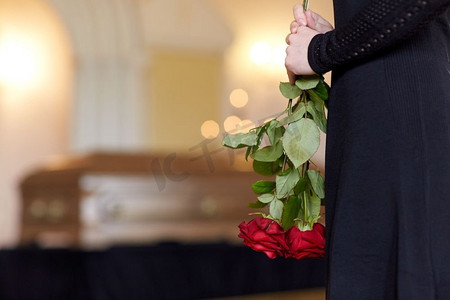 玫瑰红色摄影照片_人物和哀悼概念-教堂葬礼上手持红玫瑰和棺材的女人的特写。葬礼上手持玫瑰和棺材的妇女的特写