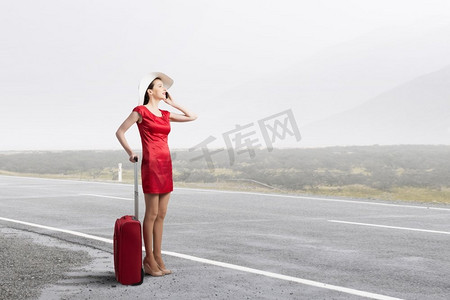 行李箱红色摄影照片_穿红衣服的女人。年轻女子在红色礼服与红色行李谈话在手机上