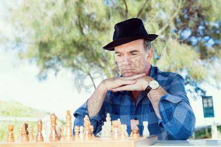 象棋游戏摄影照片_坐在户外下棋的老人。对象棋策略的思考