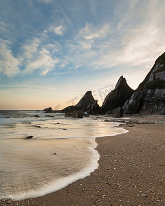 锯齿状边框摄影照片_Westcombe海滩美丽的日落风景图象在德文郡英格兰与锯齿状岩石在海滩和惊人的云形成