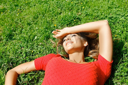 穿着红色衣服的美丽年轻女子躺在草地上。穿着红色衣服的年轻女子躺在草地上。年轻女子在红色衣服躺在草地上