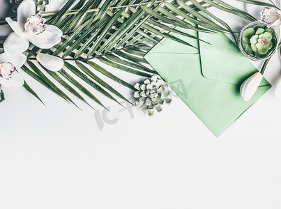 绿色与兰花、信封和多汁的装饰的热带叶子在白色桌面背景，顶视图，边界