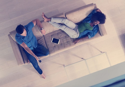 年轻的多种族夫妇在沙发上放松在豪华客厅，使用片剂和遥控器顶视图