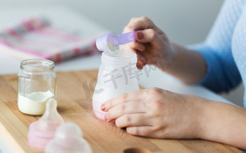 奶瓶瓶子摄影照片_食物和营养概念-母亲手持婴儿奶瓶和勺子准备婴儿配方奶。用手用瓶子和勺子制作配方奶