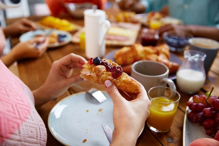 食物、烘焙与人的概念--妇女在餐桌上吃羊角面包的手。早餐吃羊角面包的女人的手