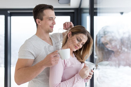 享受早晨咖啡的浪漫愉快的年轻夫妇在寒冷的冬天天的窗口在家
