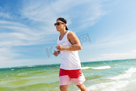 健身，运动，人和健康的生活方式理念-快乐的年轻人沿着夏天的海滩跑步。快乐的男人沿着夏日海滩跑步