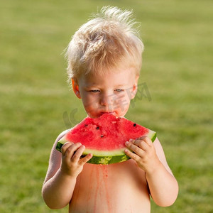 户外学步儿童的肖像。一岁男婴在花园里吃西瓜片的乡间场景。快乐孩子脏兮兮的脸。
