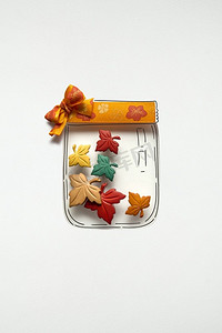 感恩节创意概念照片，白色背景上有纸做的叶子的瓶子。
