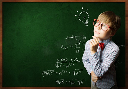 聪明的小学生。戴着红眼镜的聪明男孩在黑板上写着公式