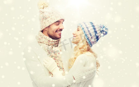 情侣衫摄影照片_冬天，时尚，情侣，圣诞节和人的概念-戴着帽子和围巾微笑的男人和女人拥抱。一对穿着冬衣的微笑情侣拥抱着