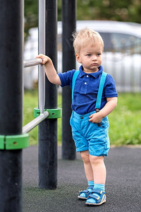 穿着短裤和吊带的蹒跚学步的孩子在户外的肖像。一岁的男婴在操场上