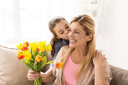 孩子给母亲摄影照片_人、家庭和假日概念-给郁金香花和亲吻她的母亲的愉快的女孩在家快乐的女孩给花给母亲在家