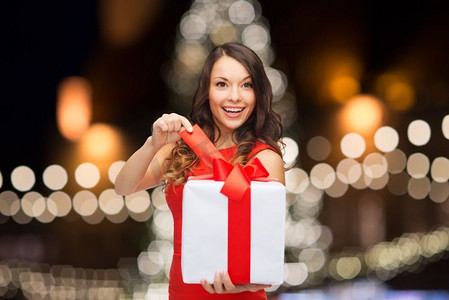 节日和人的概念-微笑的女人带着礼品盒过夜圣诞树彩灯背景。圣诞树上挂着礼品盒的女人