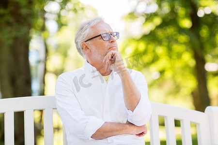 老年、退休与人的概念--一位戴眼镜、深思熟虑的老人坐在夏令营的长椅上。夏令营体贴的老人