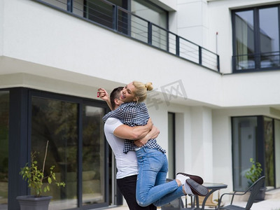 一对幸福的年轻夫妇在他们的新豪华别墅前拥抱
