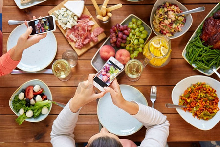 吃、人和科技概念--人们用智能手机拍摄餐桌上的食物。人们用智能手机拍摄食物