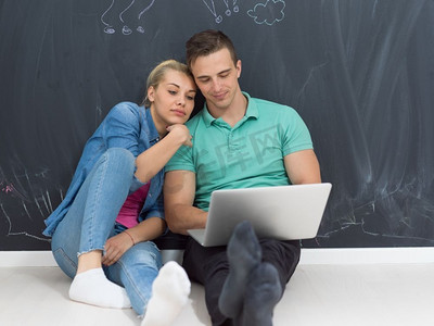 幸福的年轻恩爱夫妇在灰色黑板前使用笔记本电脑