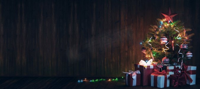 绿色的玩具摄影照片_装饰圣诞树装饰圣诞树与发光的灯和礼品盒在木背景