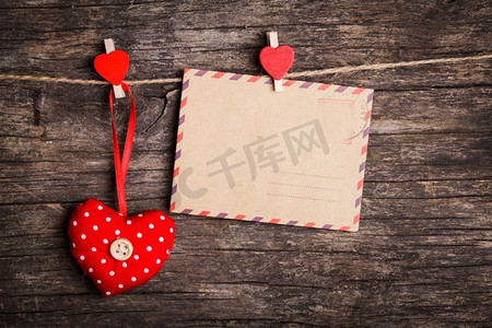 夹子挂摄影照片_红色的心形和纸牌被红色的别针挂在绳子上，质朴的背景。情人节的概念&S
