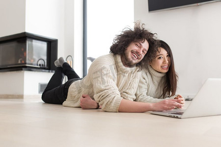 年轻漂亮的多民族夫妇在家中用笔记本电脑在地板上上网购物