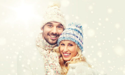 情侣衫摄影照片_冬天，时尚，情侣，圣诞节和人的概念-戴着帽子和围巾微笑的男人和女人拥抱。一对穿着冬衣的微笑情侣拥抱着