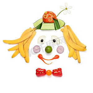 小丑巡游摄影照片_创意食品概念展示了儿童菜单中由蔬菜和水果制成的微笑小丑的肖像。
