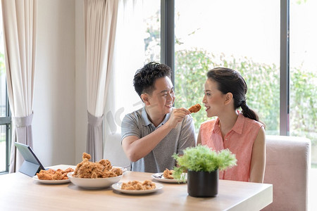 年轻的亚洲夫妇在当代住宅的客厅里一起吃炸鸡，体现现代生活方式的概念