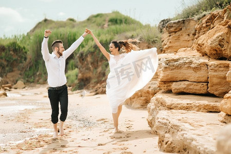 幸福的新人摄影照片_年轻的新人和新娘在沙滩上走在婚礼上