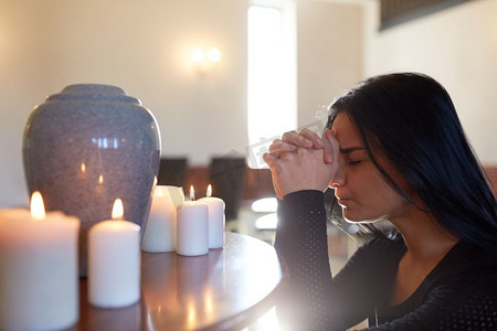 人和哀悼的概念-悲伤的女人在教堂的葬礼上用骨灰盒和蜡烛祈祷。悲伤的女人带着骨灰盒在教堂祈祷