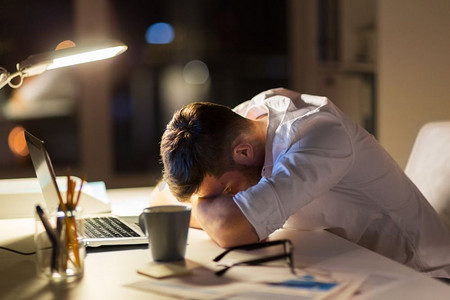 商业、超负荷工作、截止日期和人的概念-疲惫的商人躺在夜间办公室的桌子上。疲惫的商人躺在夜间办公室的桌子上