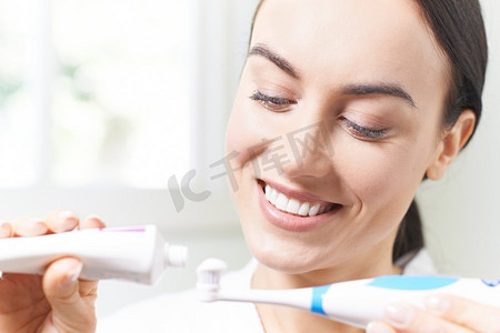一名妇女在浴室里把牙膏挤到电动牙刷上