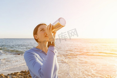 一名妇女在海滩上喝水。年轻女子在海滩上运动后喝水