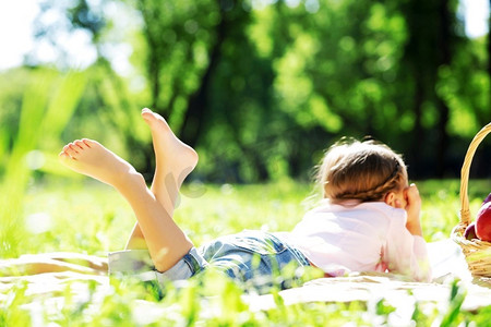 春天可爱孩子摄影照片_一个孩子躺在毯子上在夏季公园野餐。公园里的女孩