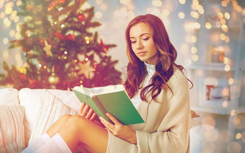 圣诞节、节假日和人的概念--快乐的年轻女子在家读书。快乐的女人圣诞节在家看书