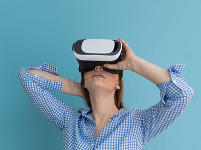 获得使用虚拟现实VR耳机眼镜的经验的愉快的女孩，在蓝色背景隔绝